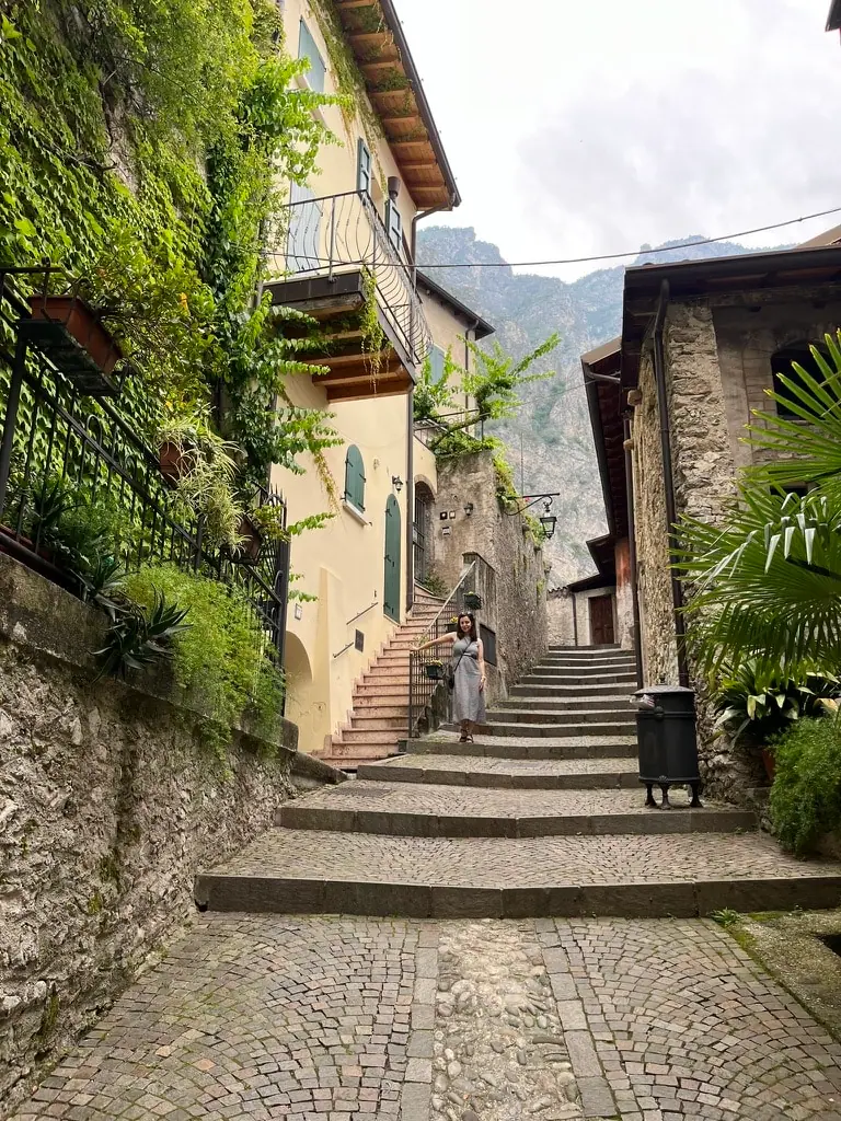Monča stojí na kamenných schodech v úzké uličce Limone sul Garda, obklopená historickými budovami.
