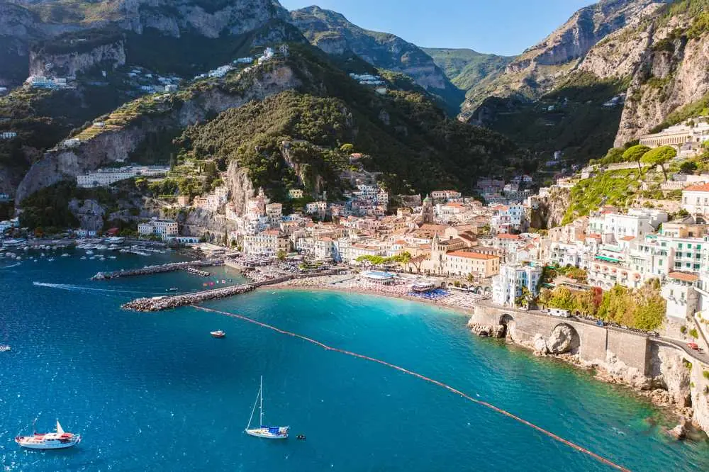 Pohled z moře na Amalfi s bílými domy tísněnými mezi skálami a tyrkysovou zátokou s jachetami