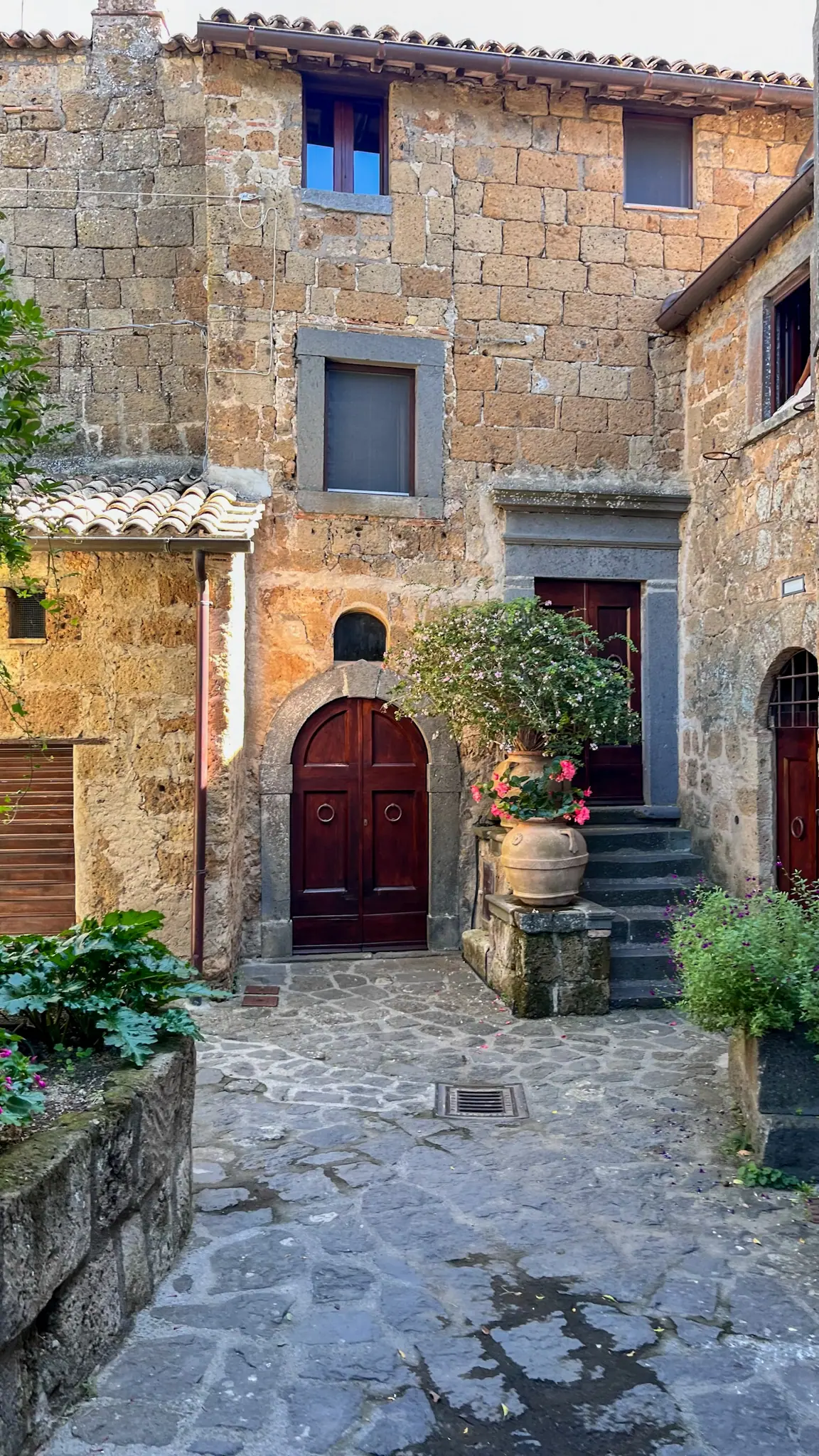 Historický kamenný dům v Civita di Bagnoregio s dřevěnými dveřmi, květinami a typickou architekturou.