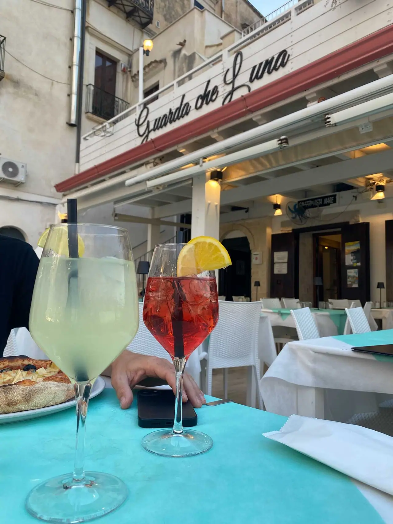 Náš večerní aperitiv v restauraci Guarda che Luna ve Vieste - dva koktejly s citronem na tyrkysovém stole před terasou restaurace