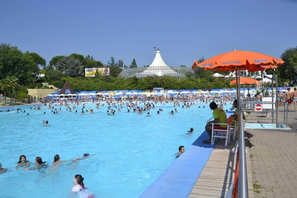 Přeplněný vlnový bazén v Aquafanu v Riccione, kde plavci splývají s tyrkysovou vodou pod rozpáleným italským sluncem.