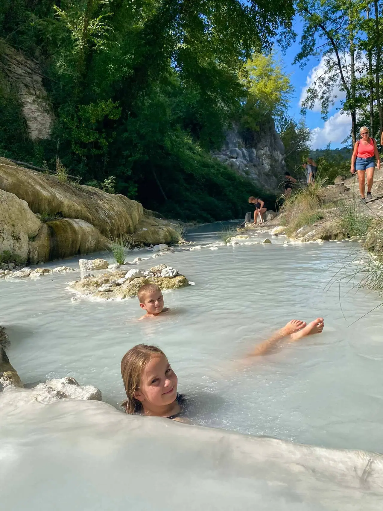Naše děti si užívají koupání v bílých vápencových bazénkách termálních lázní Bagni San Filippo v Toskánsku obklopené zelení