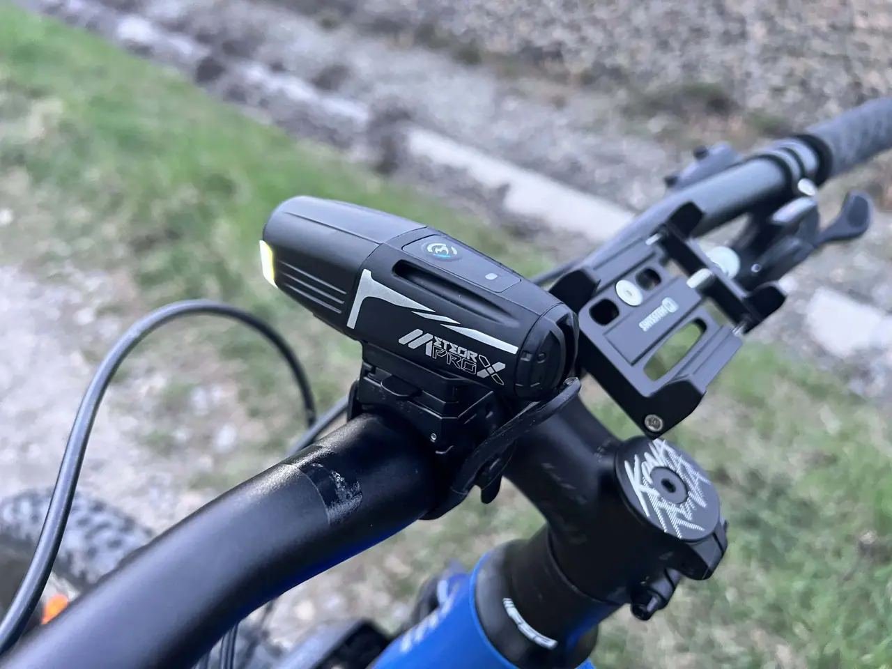 Černé cyklistické světlo Moon Meteor X Auto Pro namontované na řídítkách horského kola s phone holderem během naší testovací jízdy