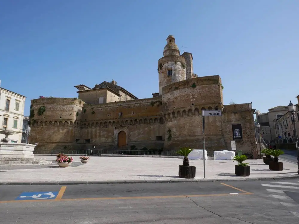 Středověký hrad Castello Caldoresco ve Vastu s masivními kamennými hradbami, kulatými věžemi a ozdobným cimbuřím na slunném náměstí
