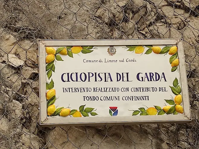 Cedulka s nápisem „Ciclopista del Garda: intervento realizzato con contributo del fondo comuni confinanti“ se zdobením citrony, typickým vzorem města.