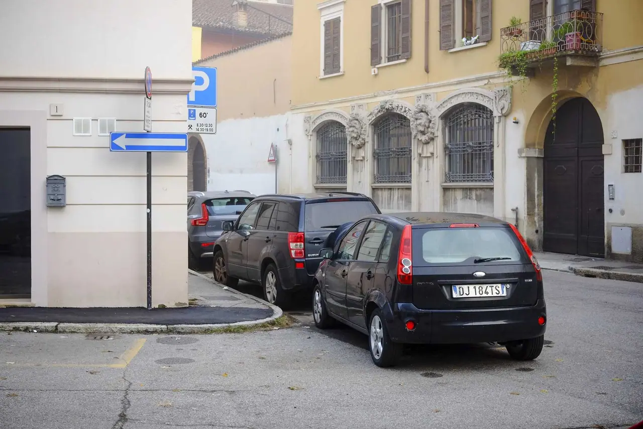 Tři tmavá auta zaparkovaná na úzké ulici v italském městě mezi historickými budovami se železnými mřížemi a balkónky
