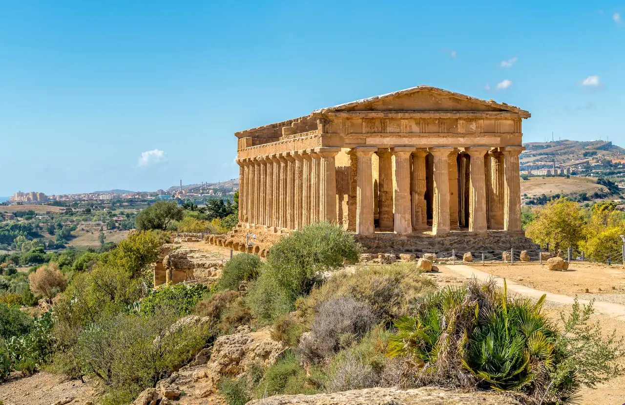 Dobře zachovalý řecký chrám Concordia v Agrigento stojí na skalnatém hřebeni obklopený středomořskými keři a olivovníky