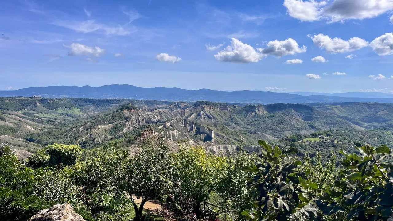 Pohled na město Civita di Bagnoregio stojící na skalním masivu s erozní krajinou calanchi v pozadí.