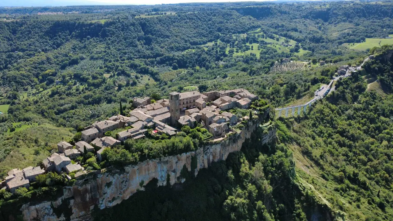 Letecký pohled na Civitu di Bagnoregio s kamennými domy na útesu propojeným úzkým mostem s okolní krajinou