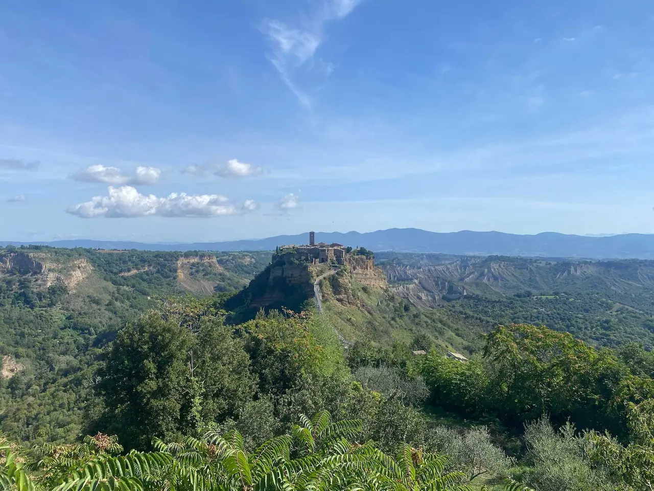 Naše fotka Civita di Bagnoregio - středověké městečko na vysoké skále spojené úzkým mostem, obklopené zelenými údolími a modrými kopci