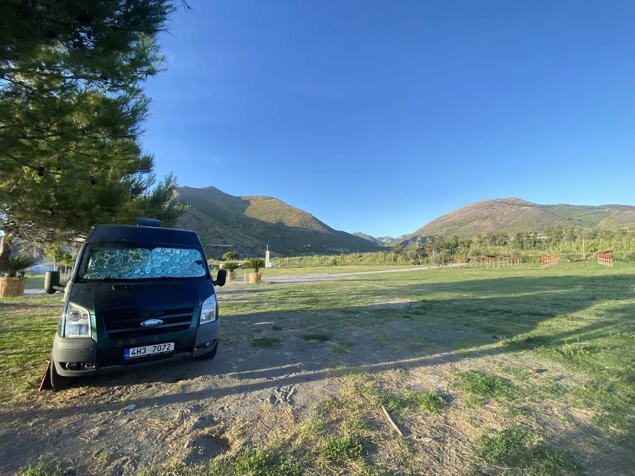 Náš Ford Transit zaparkovaný v autokempu v Maratea s výhledem na zelené kopce Basilicaty pod jasně modrou oblohou
