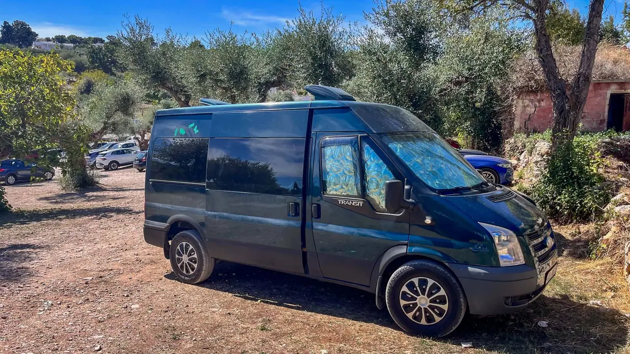 Náš Ford Transit zaparkovaný na parkovišti mezi olivovými háji u historického centra Alberobella v Apulii