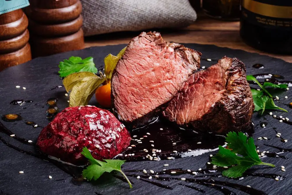 Dokonale grilovaný biftek s červeným brusinkovým pyré, zeleninou a bylinkami na břidlicové desce v elegantní restauraci