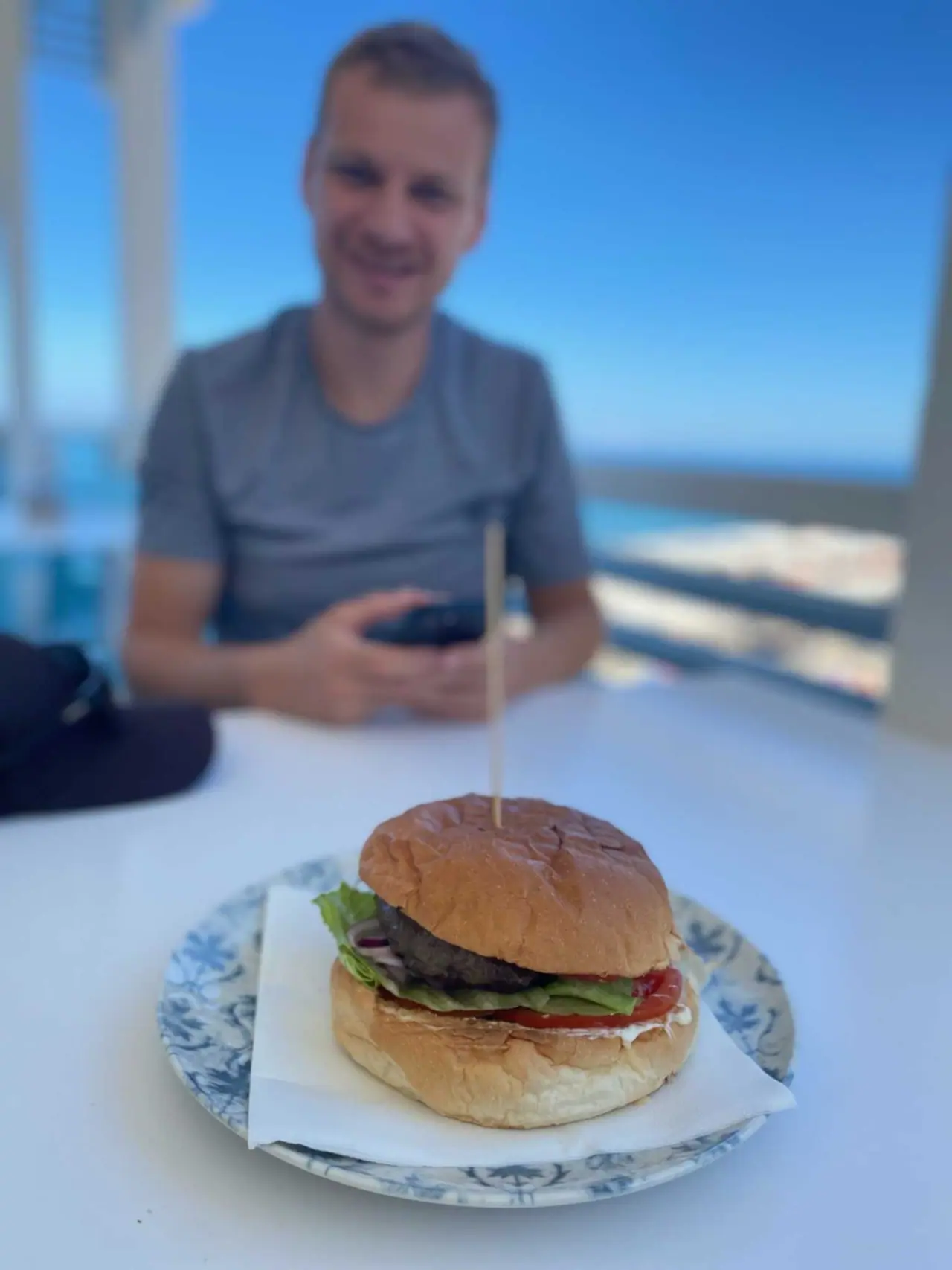 Hamburger s masovou plackou a zeleninou na talíři v restauraci v Tropea, Marťa sedí u stolu s výhledem na moře
