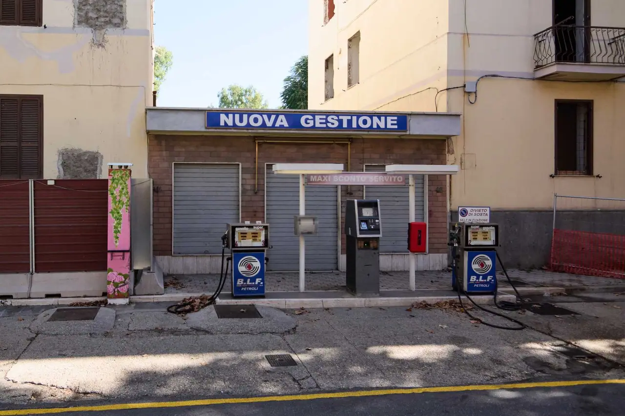 Zavřená italská benzínová stanice BLF Petroli s nápisem Nuova Gestione, zavřenými roletami a dvěma starými výdejními stojany gasolио a super.