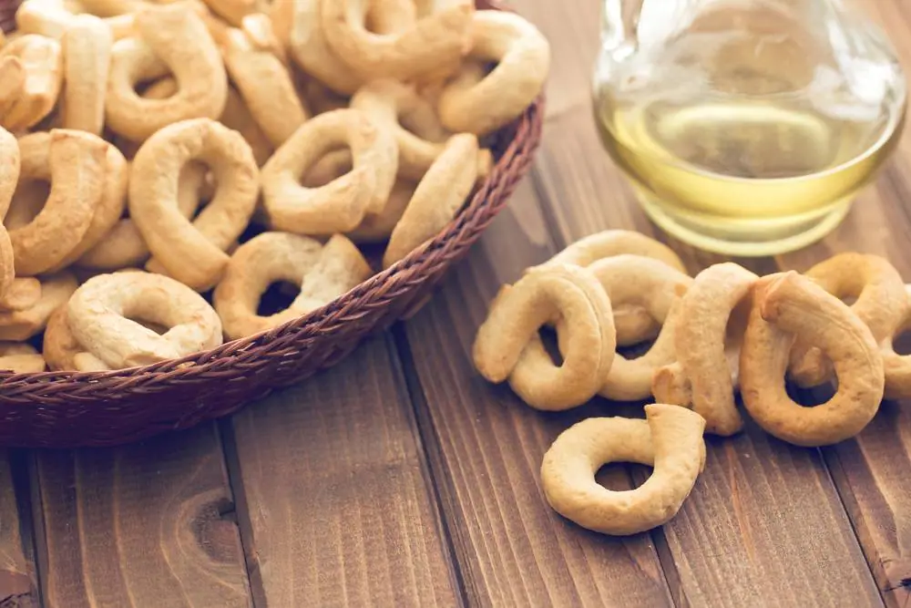 Zlatavé italské taralli v proutěném košíku na dřevěném stole s olivovým olejem v malé skleničce