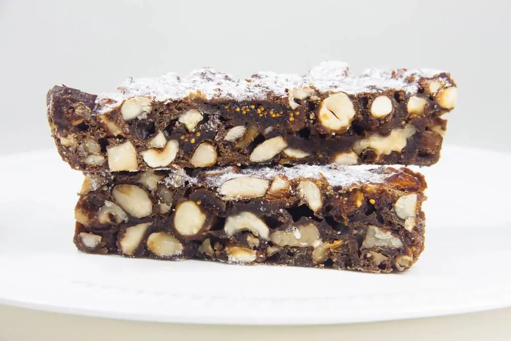Dva kousky tradičního italského panforte s mandlemi a lískovými ořechy, posypané moučkovým cukrem na bílém talíři