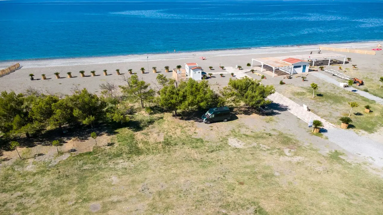 Letecký pohled na Area Camper Balai Beach Club s karavanem pod stromy, bílou pláží a tyrkysovým mořem v Kalábrii