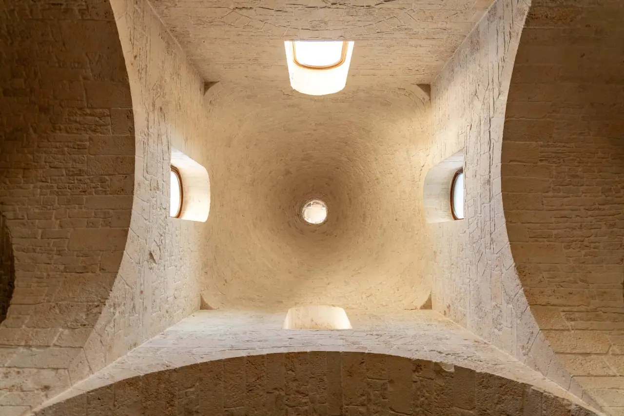 Pohled zespoda do koupelny trullo v Alberobello s kulatými okénky v bílých kamenných zdech a centrálním otvorem ve stropě