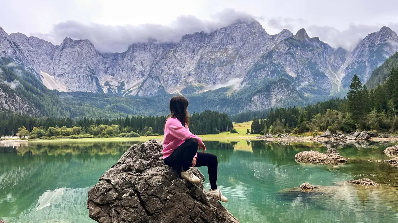Monča sedící na kameni u Lago di Fusine Superiore s výhledem na hory