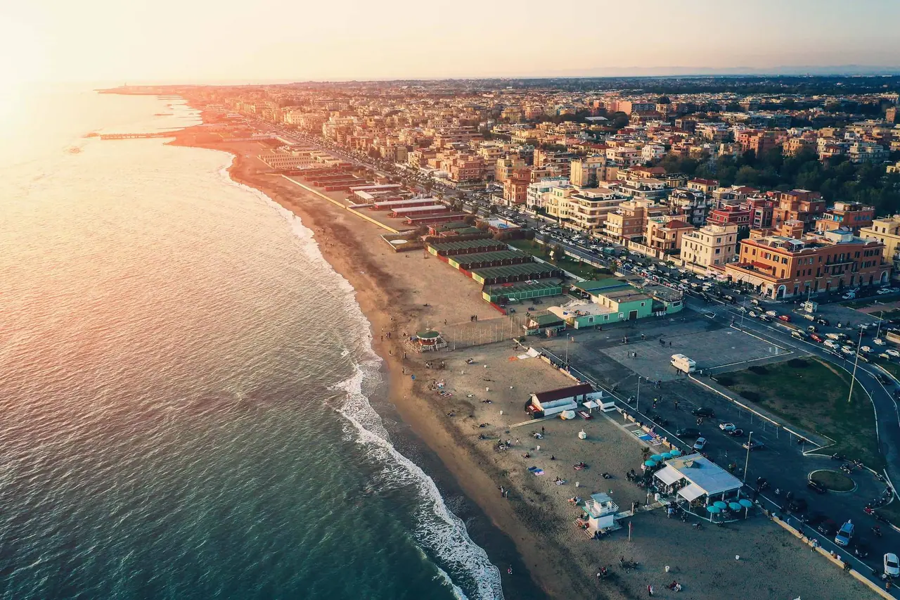 Letecký pohled na Lido di Ostia při západu slunce, kde zlaté světlo zalévá písčitou pláž lemovanou hustou zástavbou římského přímořského letoviska.