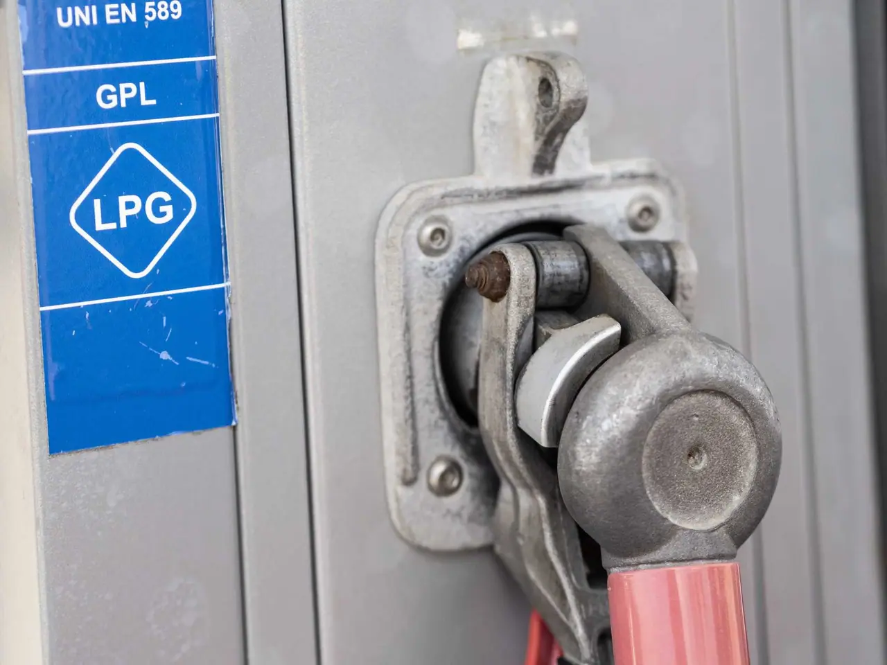 Zblízka záběr kovové pistole LPG u čerpací stanice v Itálii s modrou etiketou GPL a normou UNI EN 589