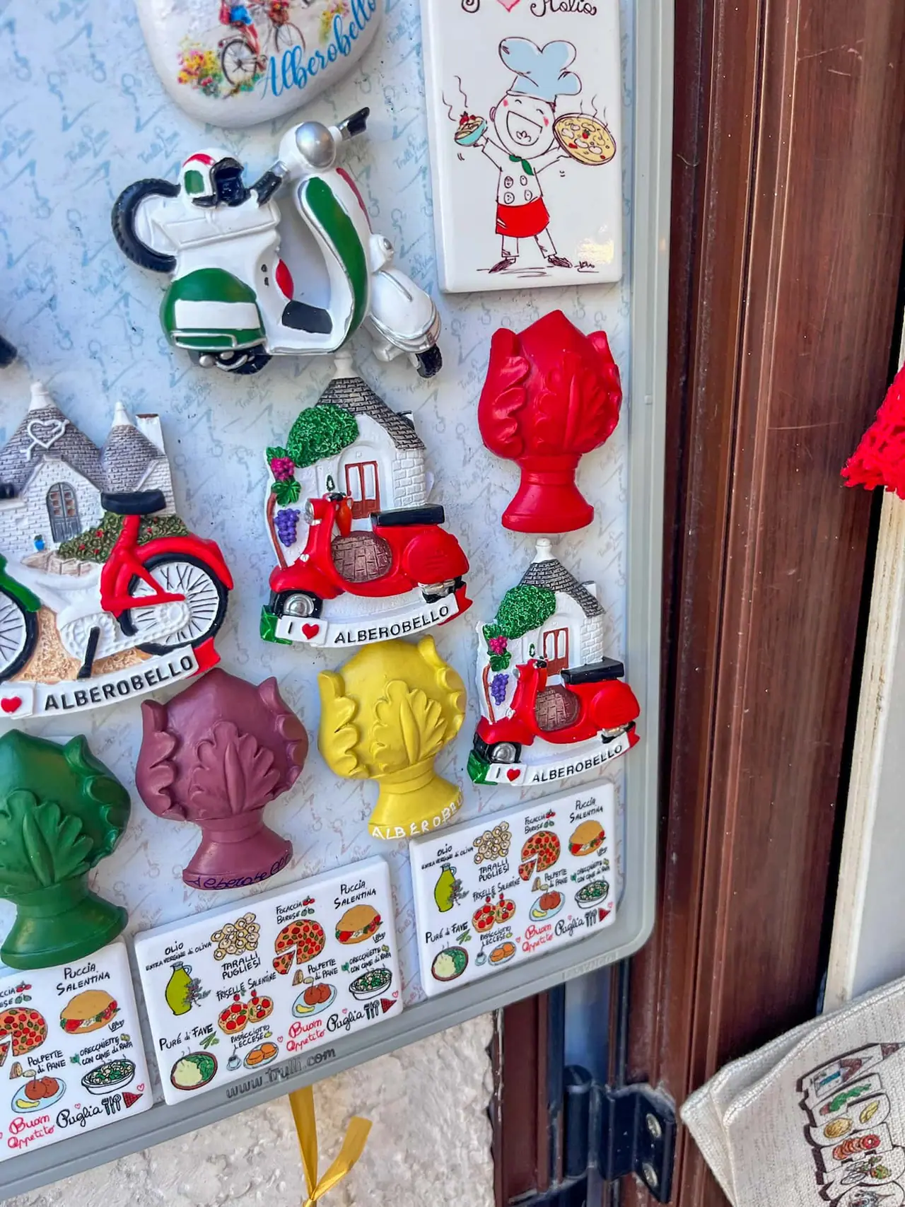 Barevné magnetky a suvenýry s motivy Alberobella, trulli domečků a italských Vesp na turistickém stánku