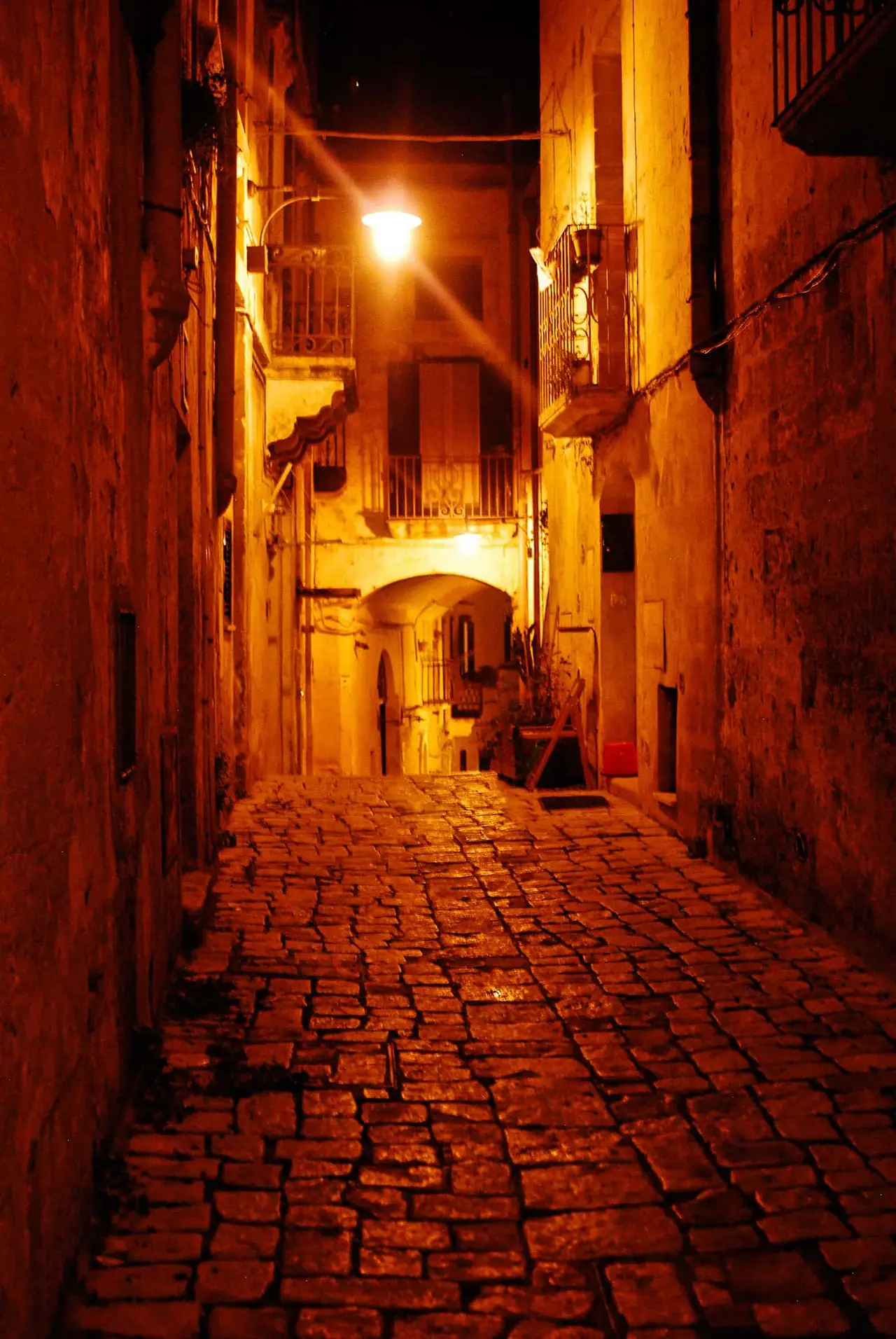 Úzké kamenné uličky historické čtvrti Sassi di Matera osvětlené teplým světlem pouličních lamp a oken domů po setmění