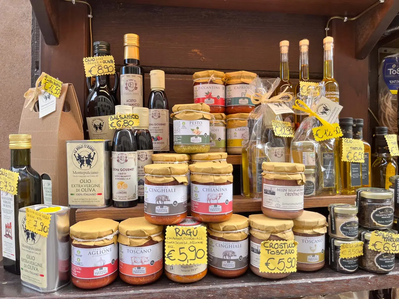 Regál plný toskánských specialit v Montepulciano - olivový olej, ragù, pesto a místní delikatesy s cenovkami v eurech