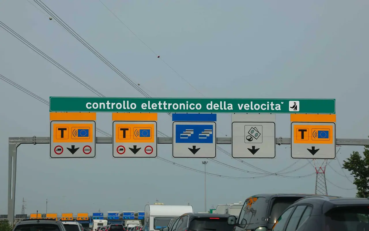 Nad dálnicí visí zelená tabule s nápisem kontrollo elettronico della velocita a barevnými značkami pro jednotlivé pruhy