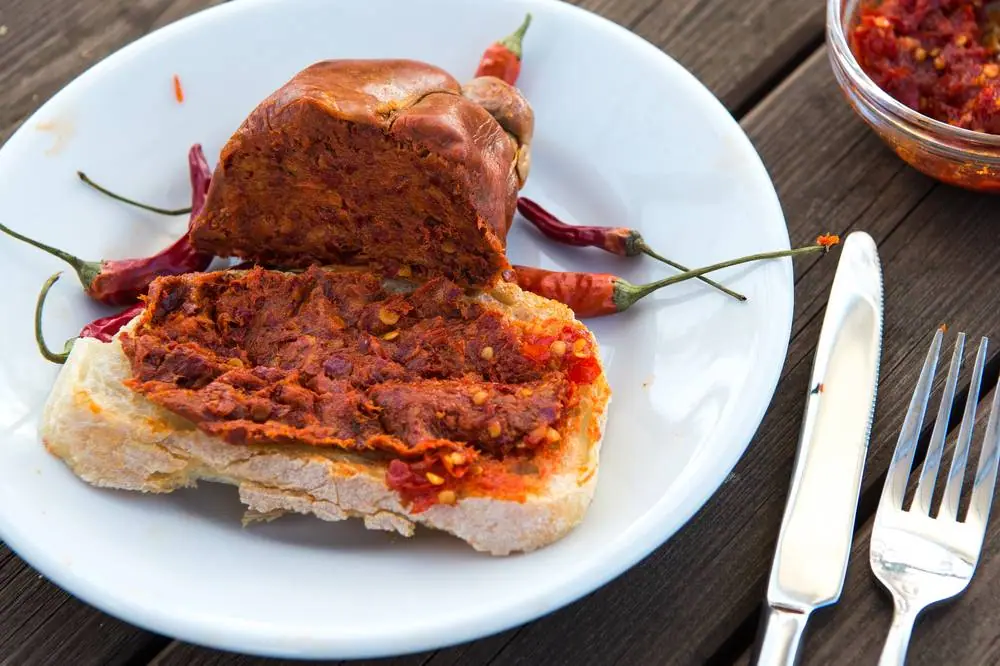 Tradiční kalábrijská nduja rozetřená na chlebu s chilli papričkami na talíři, ostrá červená pomazánka s klobásou