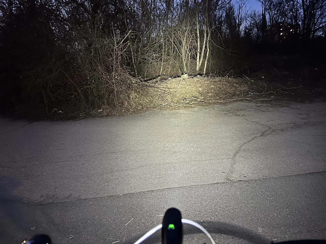Náš test cyklistické lampy Moon Meteor na večerní cestě - světelný kužel osvětluje asfaltovou cestu a okolní křoví