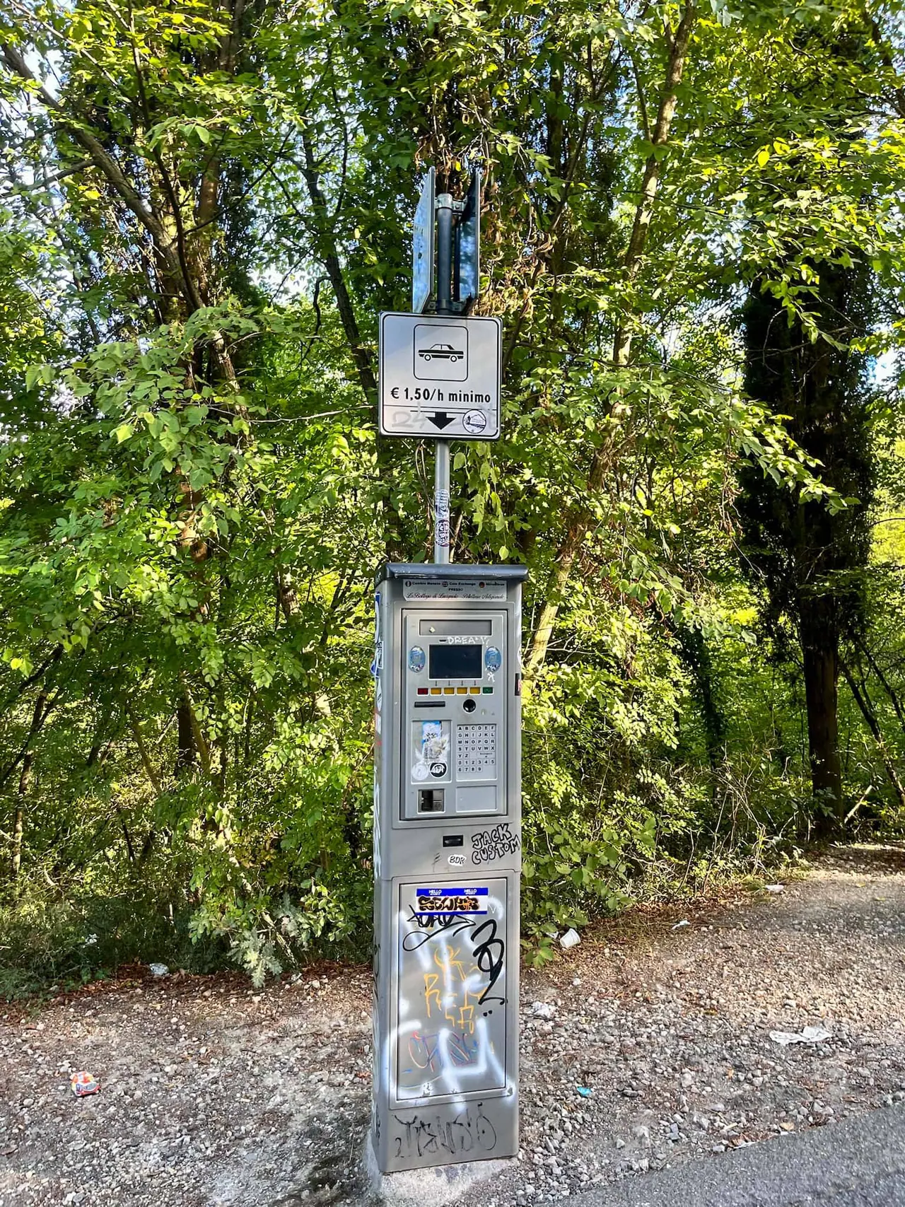 Šedý parkovací automat s cenou 1,50 eur za hodinu stojí mezi zelenými stromy v lázeňském městečku Bagni San Filippo v Toskánsku