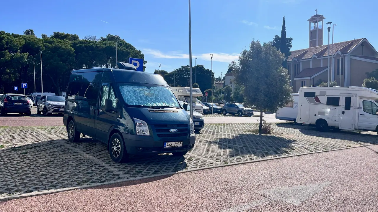 Dodávka a obytné vozy na parkovišti u kostela