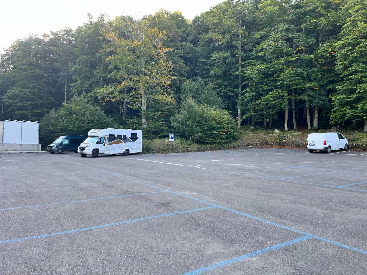 Parkoviště u horského rifugia s obytným vozem a dodávkami, v pozadí husté lesnaté svahy toskánských kopců
