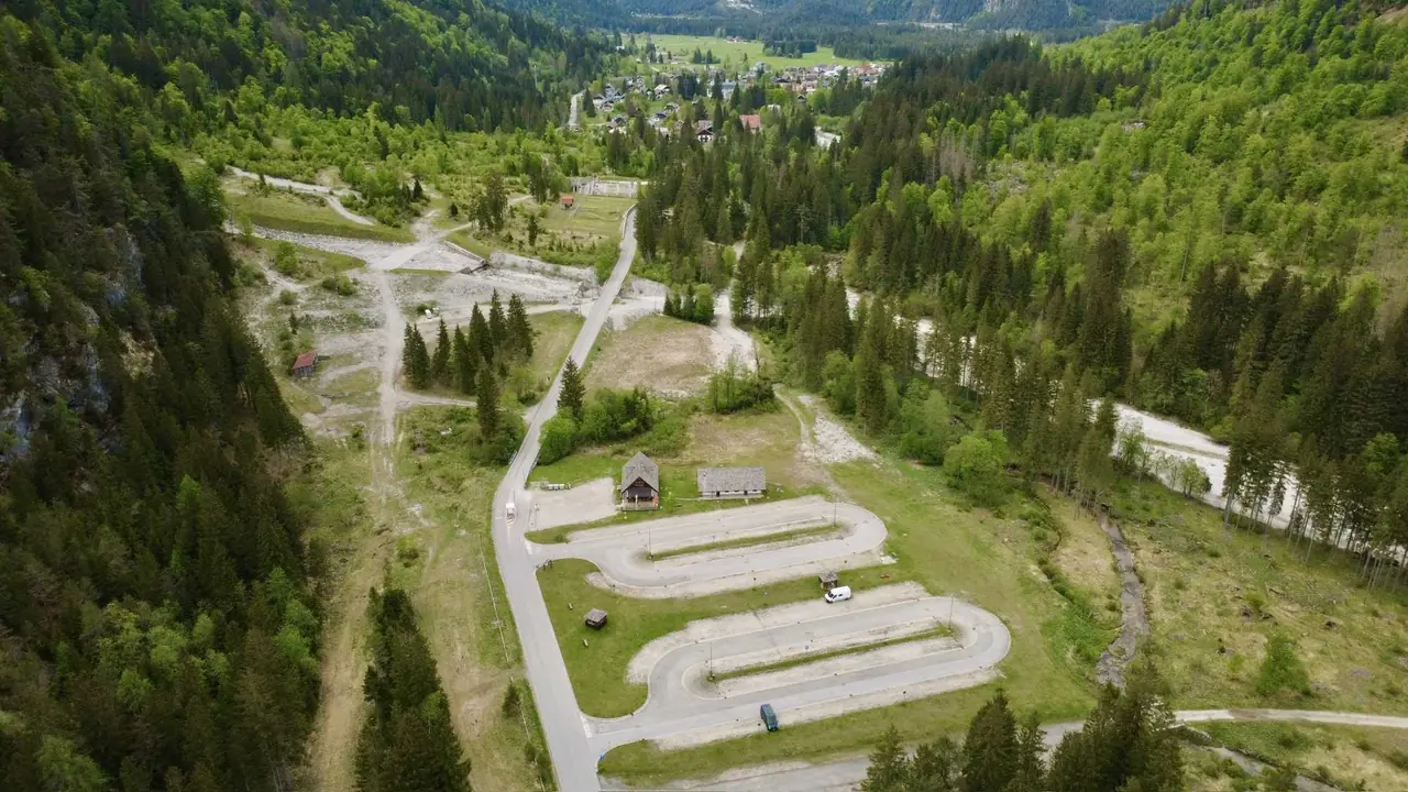 Letecký pohled na parkoviště u vstupu do údolí Val Saisera obklopené jehličnatými lesy a horami poblíž Malborghetto-Valbruna.