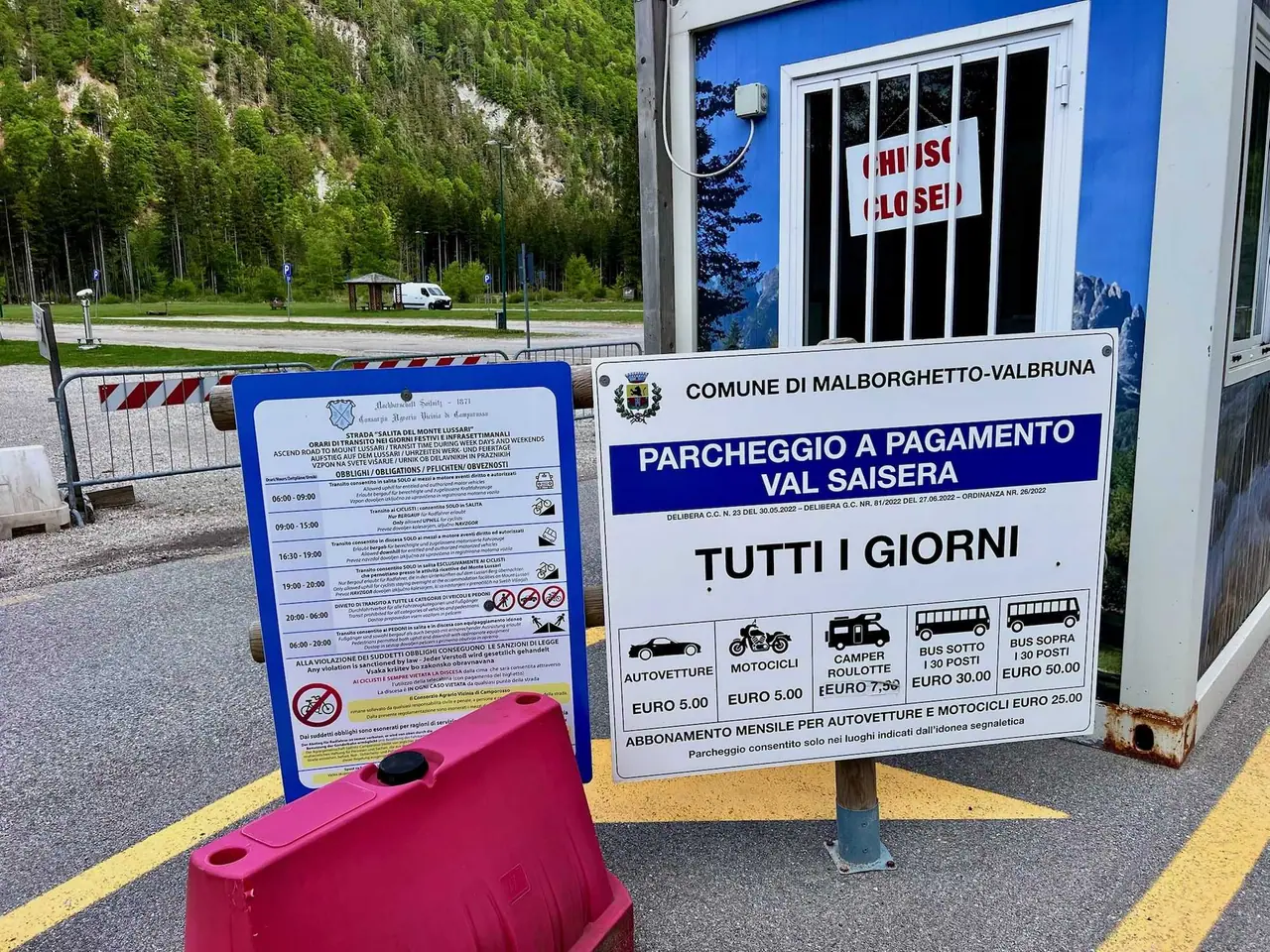 Placené parkoviště Val Saisera v Malborghetto-Valbruna s cenovníkem pro auta za 5 eur, na pozadí zelené Julské Alpy.