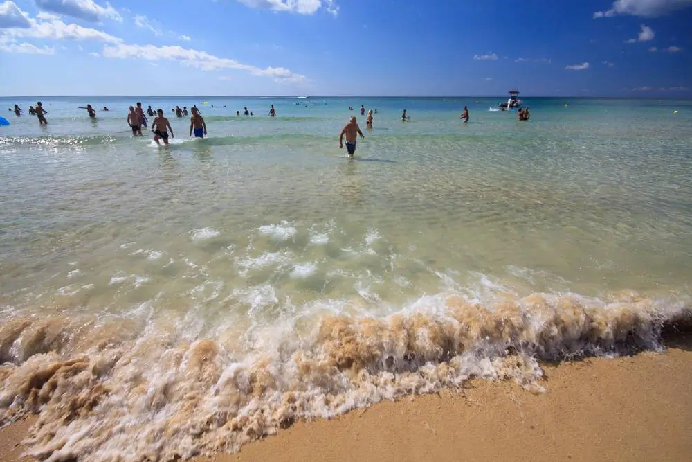Průzračné tyrkysové moře v Pescoluse na Salentu, kde se turisté brodí po písčitém dně za slunečného dne