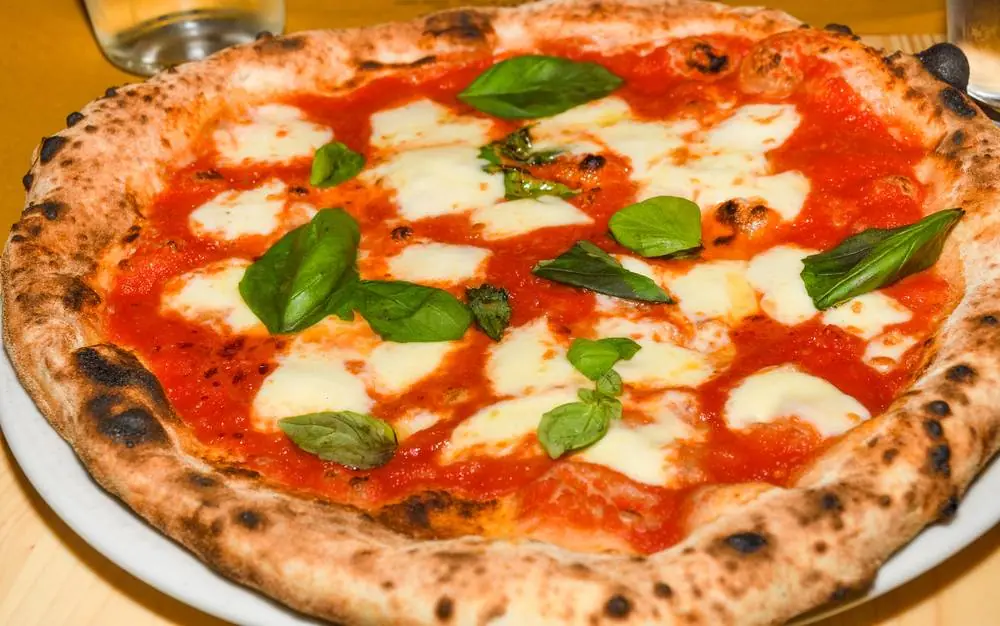 Čerstvě upečená pizza Margherita s mozzarellou, rajčatovou omáčkou a čerstvou bazalkou na bílém talíři v italské restauraci