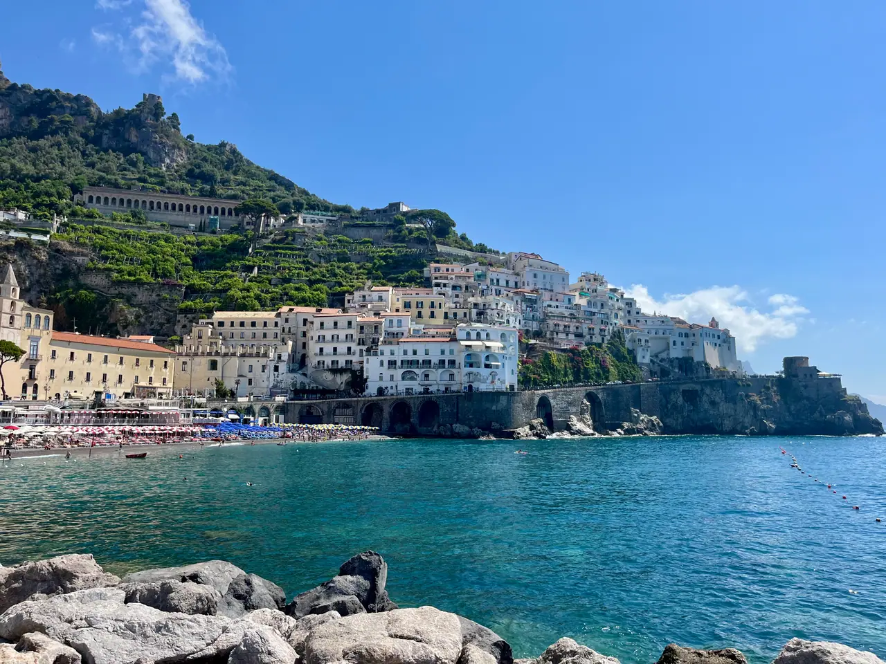 Pláž v Amalfi s barevnými domy na svahu a tyrkysovým mořem