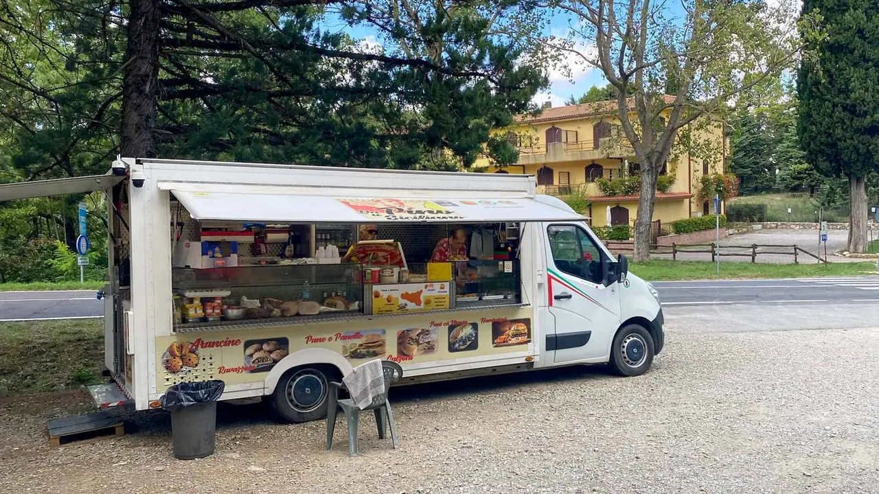 Bílý pojízdný obchod s občerstvením parkuje u silnice v Bagni San Filippo mezi zelenými stromy a žlutými domy