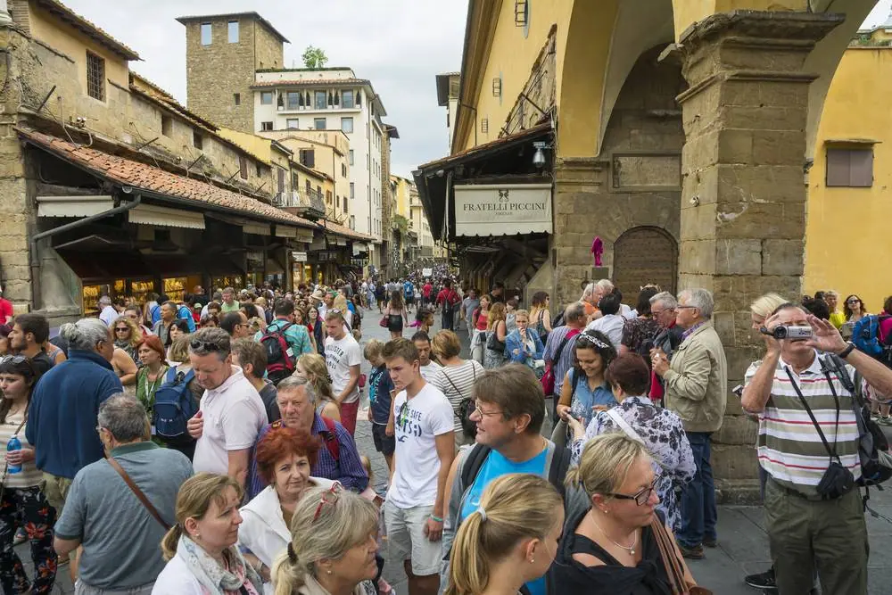 Přeplněný Ponte Vecchio ve Florencii, stovky turistů tlačí se kolem zlatnických obchodů včetně Fratelli Piccini za letního dne