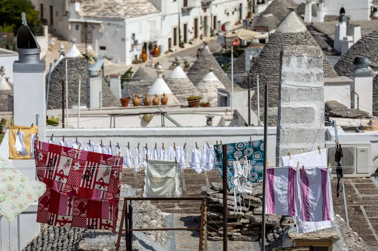 Barevné prádlo visí na šňůrách mezi bílými budovami s typickými kamenými střechami trulli v Rione aia Piccola