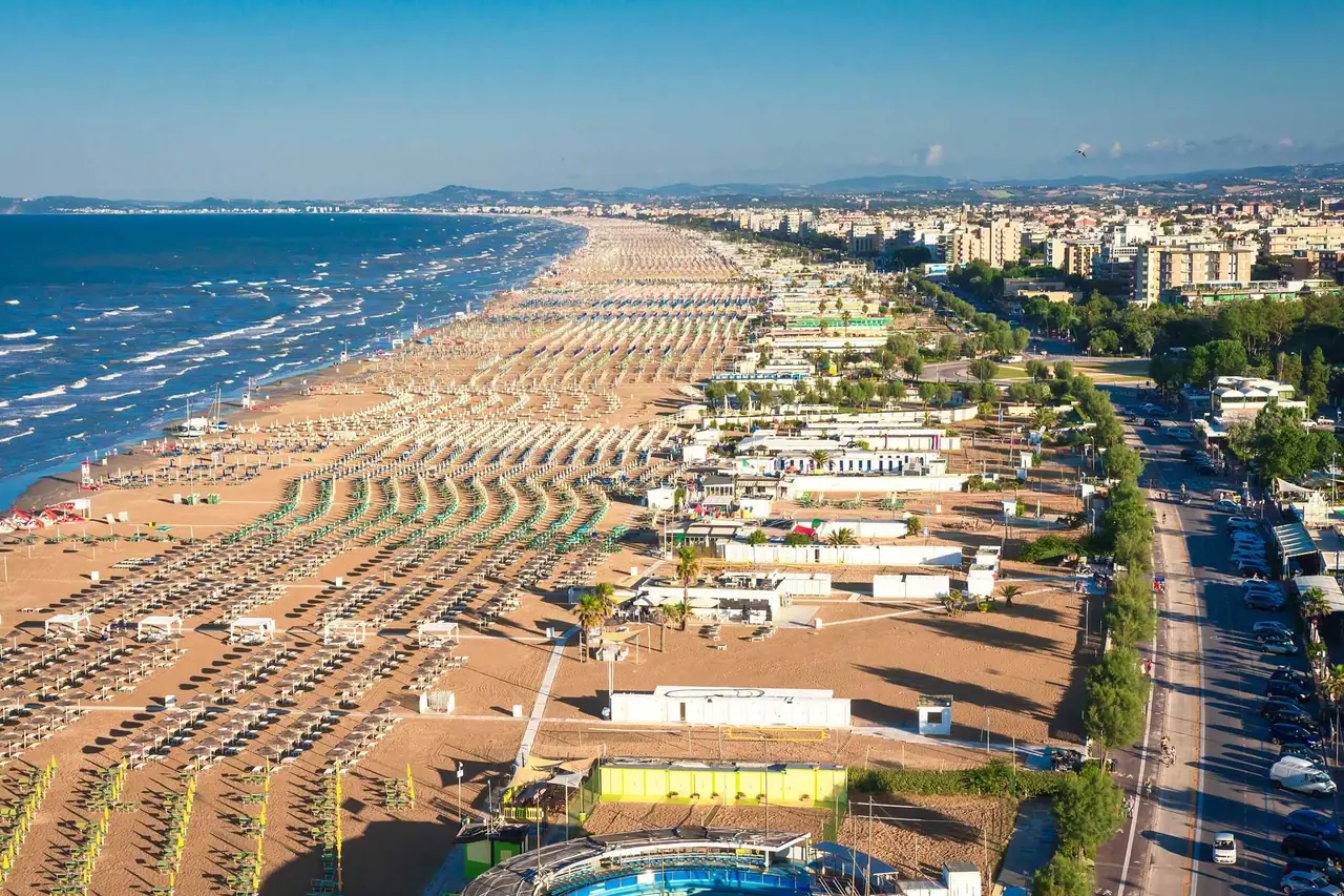 Letecký pohled na pláž Rimini s nekonečnými řadami slunečníků a lehátek podél pobřeží Jaderského moře