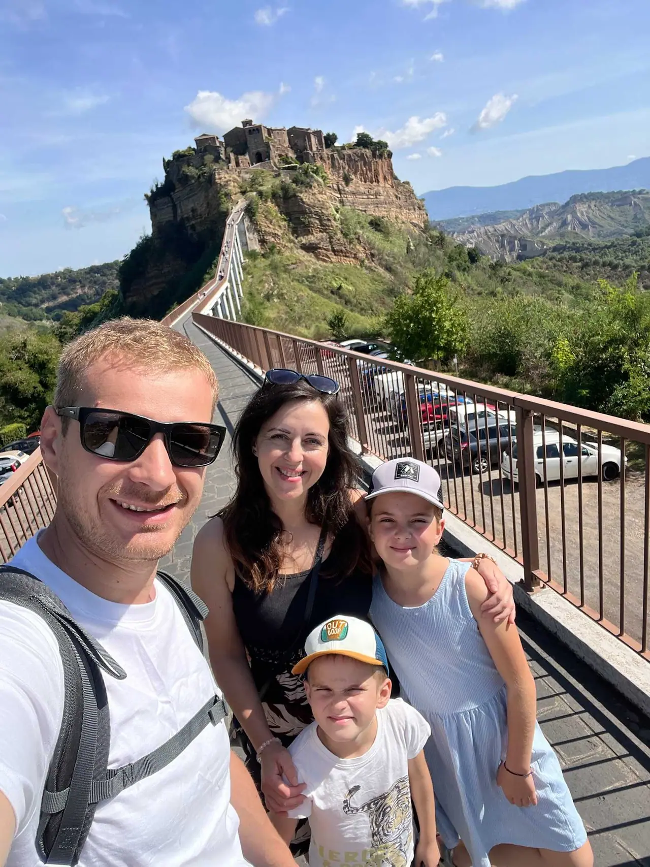 Rodinné selfie na dřevěném mostě vedoucím do Civita di Bagnoregio s výhledem na starověké město na tufovoé skále