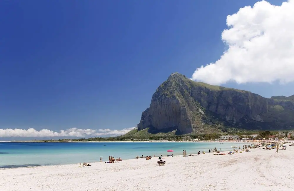 Bílá písčitá pláž San Vito lo Capo na Sicílii s tyrkysovým mořem a mohutnou skalnatou horou Monte Monaco v pozadí