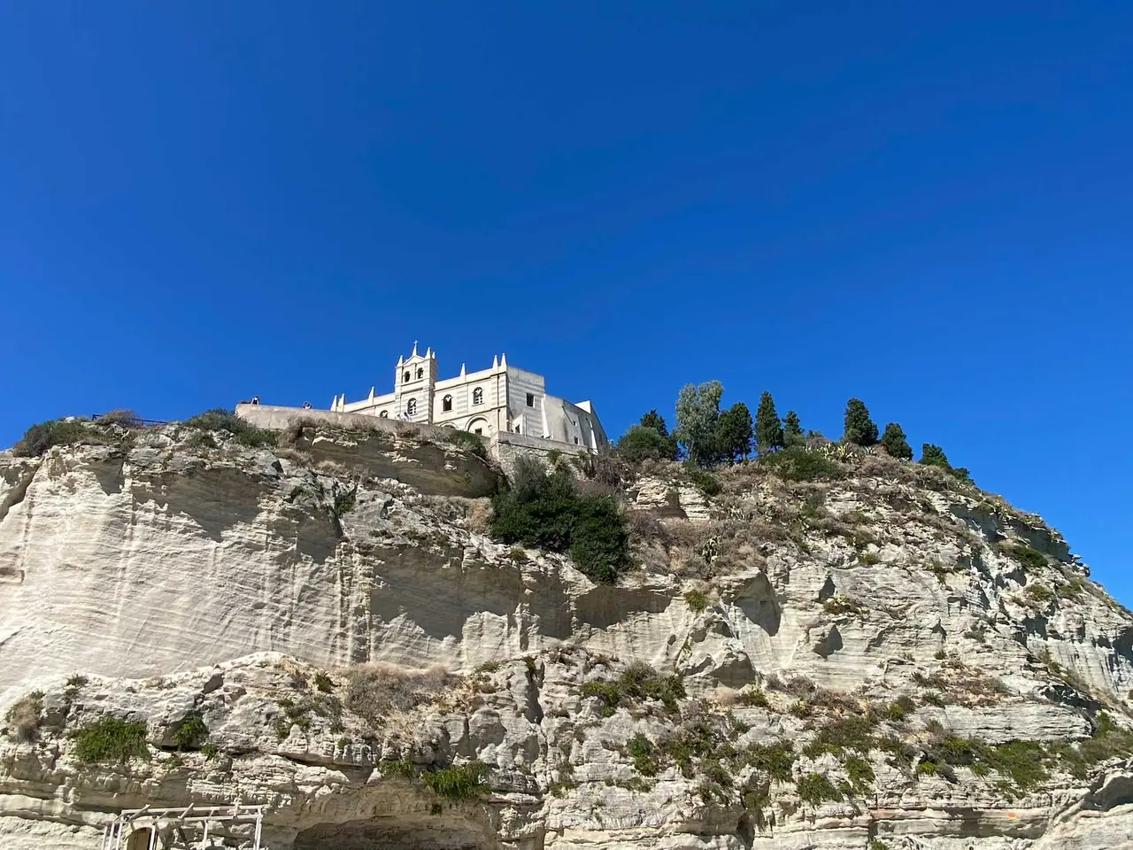 Benediktínský klášter Santa Maria dell'Isola na pískovcové skále nad mořem v Tropei, bílá stavba s věžemi na dramatických útesech