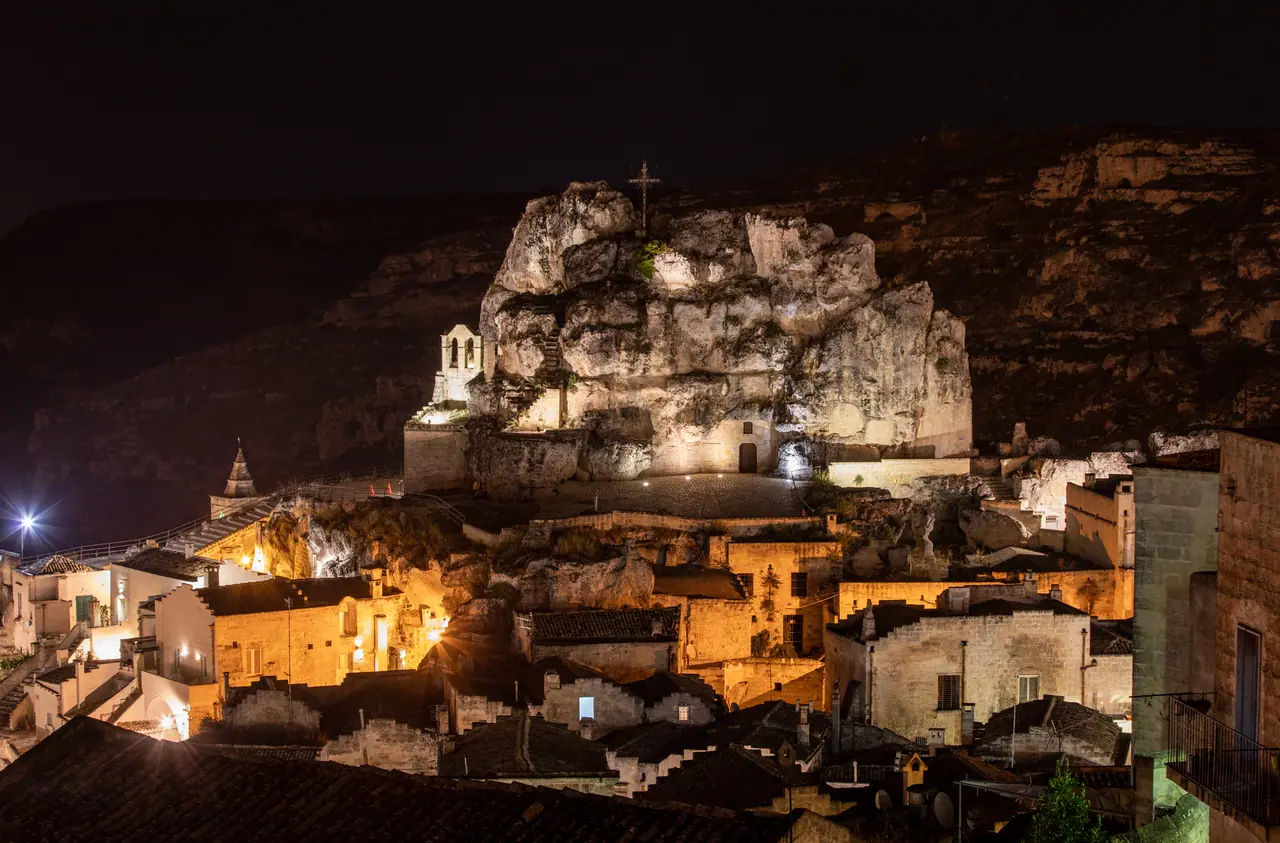 Večerní pohled na nasvícený kostel Santa Maria de Idris vytesaný ve skále uprostřed historické Matery