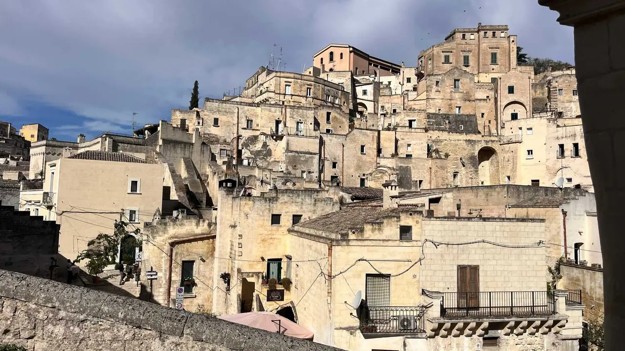 Kamenné domy vytesané do skály v Sassi di Matera s typickými balkónky a úzkými uličkami pod oblačným nebem