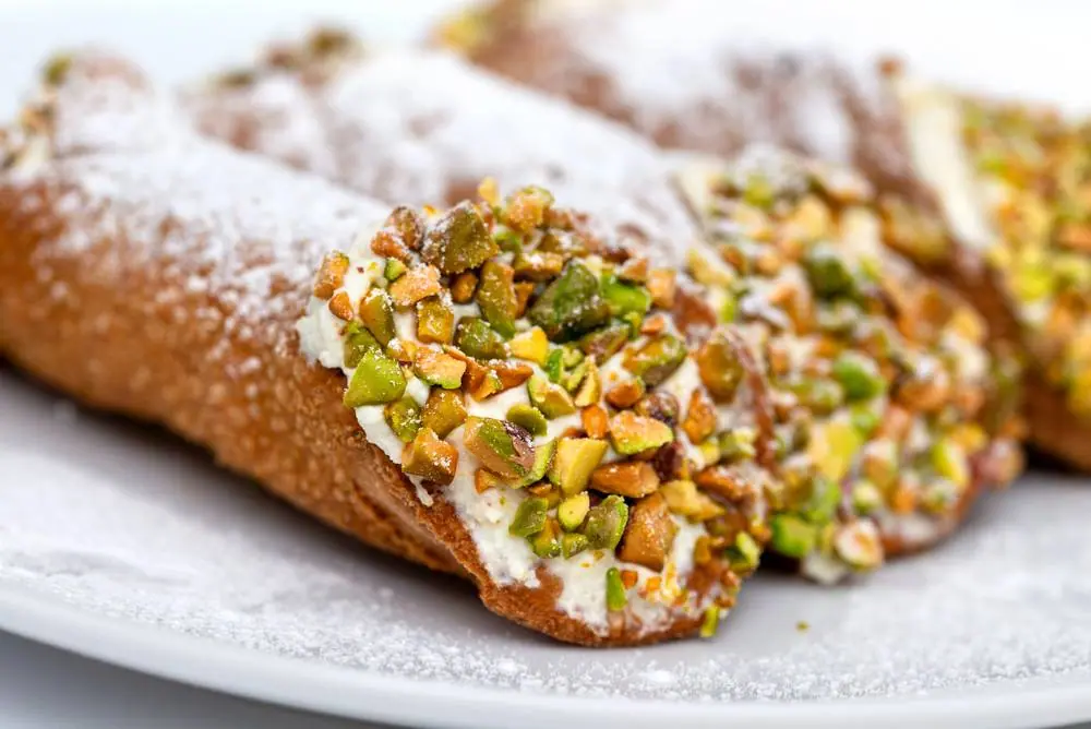 Čerstvé sicilské cannoli plnené ricottou a posypané drobnými pistáciemi na bílém talíři, tradiční italský dezert